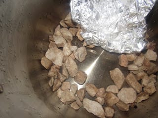 stones laid on the bottom of a pot with aluminium foil hanging above